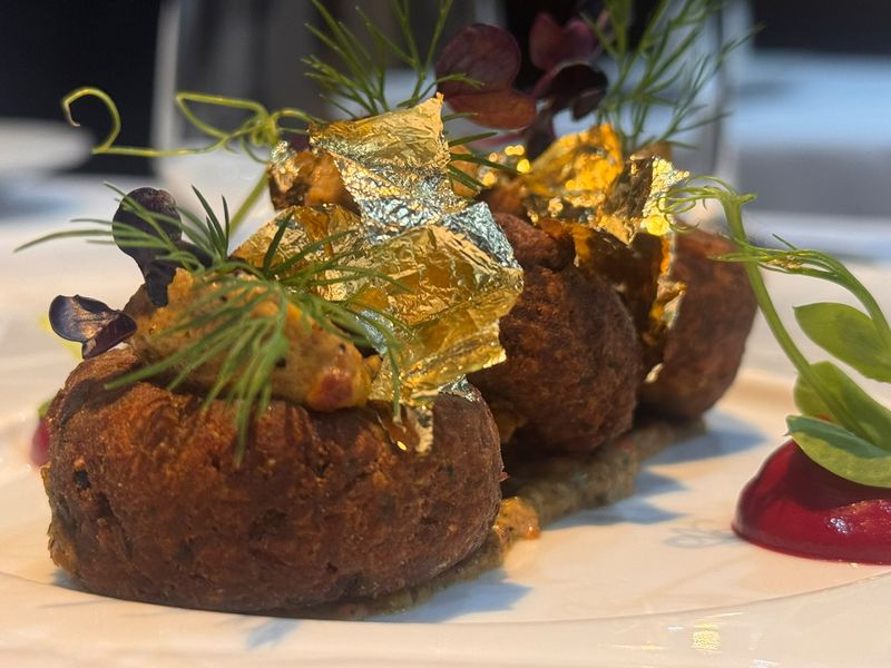 A plated dish finished with gold leaf, dill, micro herbs and a beetroot purée